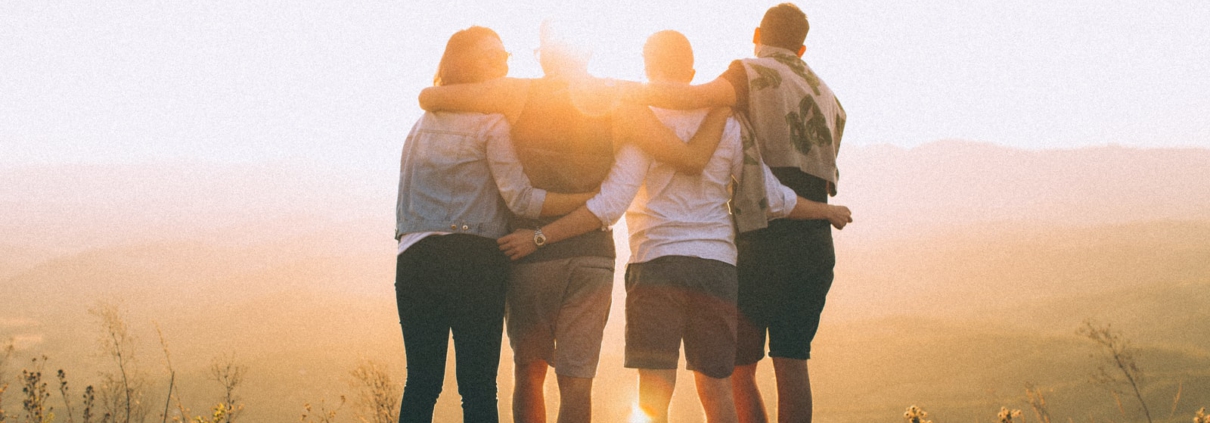 four person hands wrap around shoulders while looking at sunset